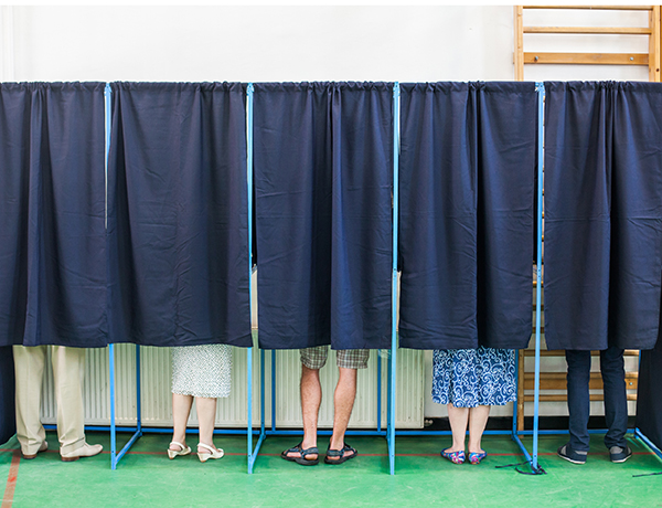 a group of people standing behind a row of blue voting booths