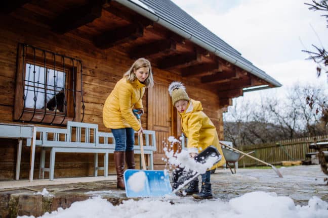 two children shoveling snow in front of a cabin